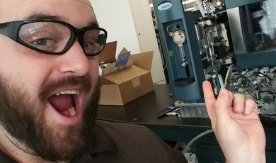 A man wearing glasses points at a machine with an excited look on his face