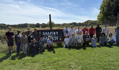A group stands in front of a Share the Harvest Sign