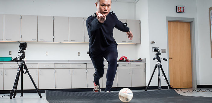 a student in the biomechanics lab wearing all black with little velcro white balls attached to his clothes bowling on a mat with cameras around him
