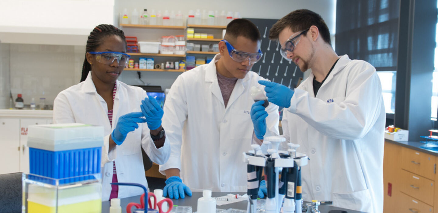 3 students in a lab looking at liquids at a table with equipment on it