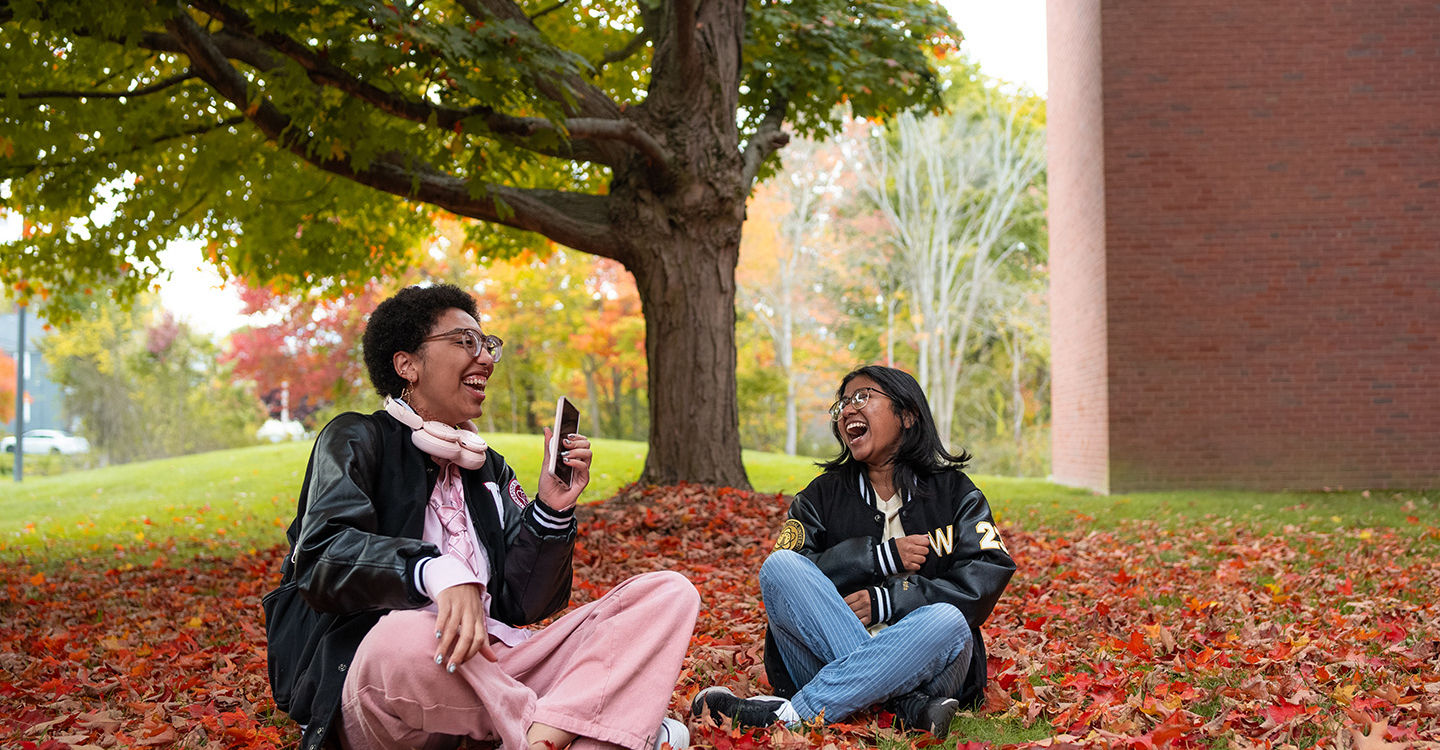 Two students sitting among red leaves under a tree on BSU's campus