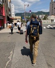 Collin Asmus walking down a street away from the camera with a large back pack on and mountains in the distance