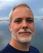 headshot photo of Dr. Matt Bell with ocean, sky and boats in background