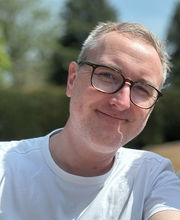 Dr. James Pearson smiling, balding with short gray hair, wearing large black rimmed glasses and a white t-shirt