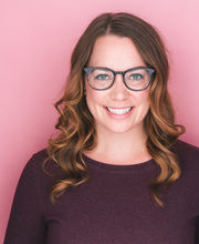 Sarah Bedard smiling with long wavy light brown hair and wearing large rimmed glasses and a long sleeve plum colored jersey