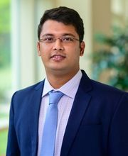 Dr. Avinandan Chakrabort with short, dark brown wavy hair wearing rimless glasses and a blue blazer over a white button up shirt with a light blue tie