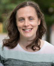 Dr. Robin Dawson smiling with long brown hair and wearing a long sleeve top with wide horizontal bands of white, light blue and gray