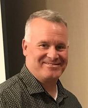 Christopher D. Delmonte smiling with balding short gray hair and wearing a black and white button down shirt