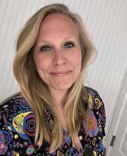 Dr. Samantha Ewart smiling with long dirty blonde hair wearing a v-neck top with black background and colorful design