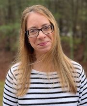 headshot photo of Holly Ferreira with long straight dirty blonde hair, wearing black rimmed glasses and a white and black striped jersey