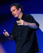 Al Forgione on stage talking with short wavy dark brown hair, wearing a button up short sleeve black shirt