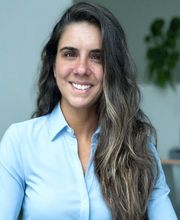 Ashley Harris smiling with long wavy dark brown hair with highlights and wearing a light blue long sleeve button down top