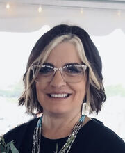 Dr. Kim MacInnis smiling with dark brown hair and a blonde strip around her face wearing black and white rimmed glasses and a black top