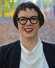 Dr. Melanie McNaughton with short dark brown hair wearing black rim round glasses, a white blouse and black jacket