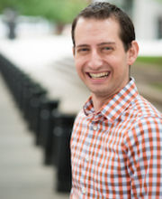 Dr. Seth Meyer looks at the camera and smiles in a red and blue checkered shirt outside