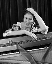 black and white photo of Dr. Deborah Nemko smiling at her piano with short dark brown hair