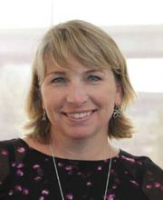 Karen Norton smiling with medium length dirty blonde hair and wearing a black blouse with pink flecks on it