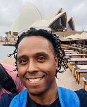 Pedro Suncar smiling with medium length black braids. Sydney Australia's opera house is in background