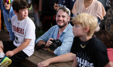 Doug Breault holds a camera as he is surrounded by young campers.