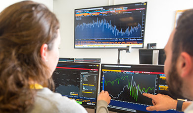 People collaborate at computers showing financial markets.