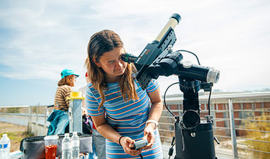 A student looks in a telescope at the sun from a roof deck.