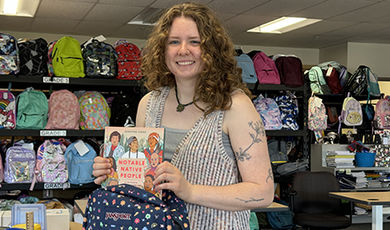 Hanley places a book in a backpack while standing in front of shelves filled with backpacks.