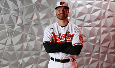 A man stands with his arms crossed wearing a baseball uniform