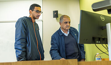 A professor and student work at a computer.