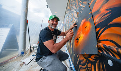 Mark Carvalho applies spray paint to the mural using a stencil.