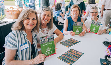 Four people sit at a table holding Senior College brochures.