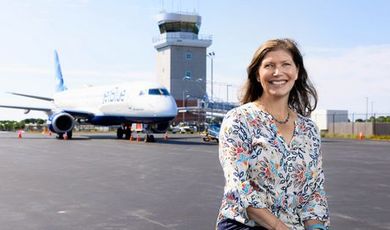 Kate Servis stands on the airport tarmac with a jet and the control tower behind her.