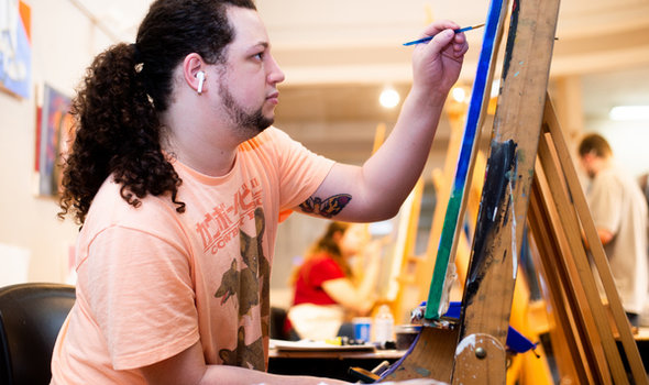 a BSU student sitting at an easel painting with other students painting at easels in the background