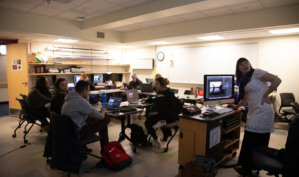 Professor Amy Lovera showing and talking about a photo on a screen while students follow along on their laptops