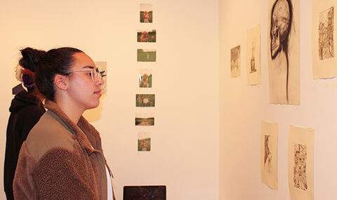 a woman looking at drawings hanging on a wall in the BSU Wallace Anderson Art Gallery