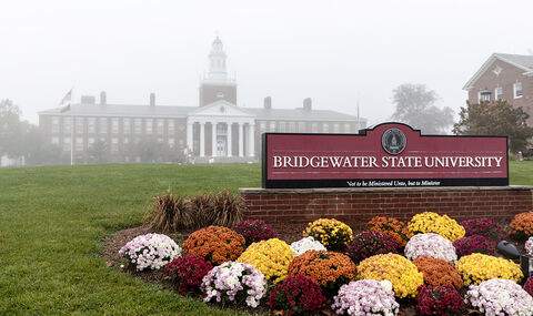 The Bridgewater State University sign on Boyden Quad with fresh fall mums; Boyden Hall is in the fog in the background