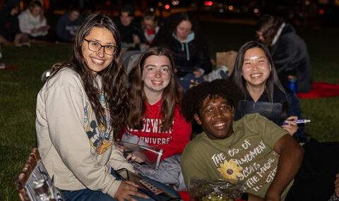 Four students smiling together, outside on the Boyden Quad, playing giant bingo