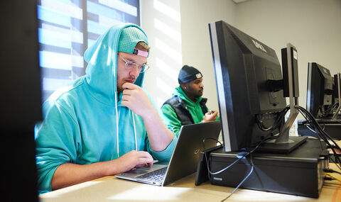 Two students working on laptops and computer workstations in a cybersecurity class