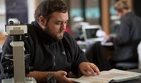a student sitting at a table with a microscope looking at an open book