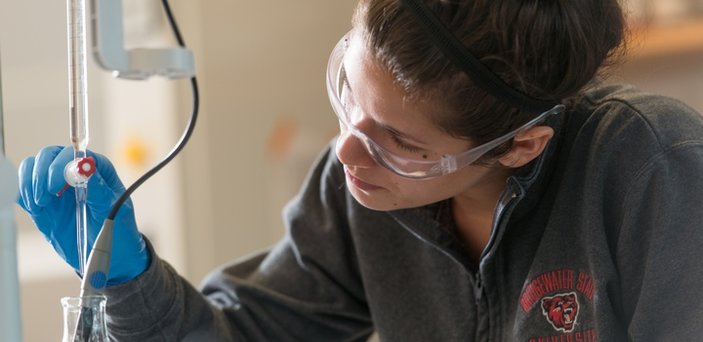 A student wearing rubber gloves and safety glasses while using equipment in chemistry lab