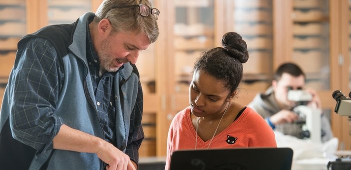 Professor Michael Krol showing something in a book to a student in geology lab