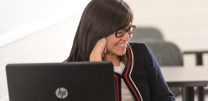 student at desk with laptop in class smiling