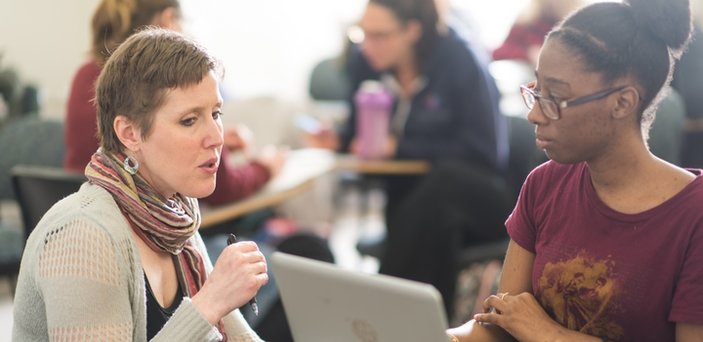 Professor speaking to a student at the student's desk and computer