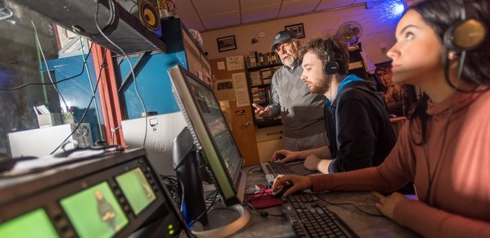 Students wearing headphones working in front of computers and looking at television monitors. A professor speaks while they work.