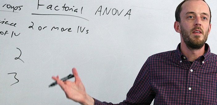 A professor speaking to a class in front of a white board