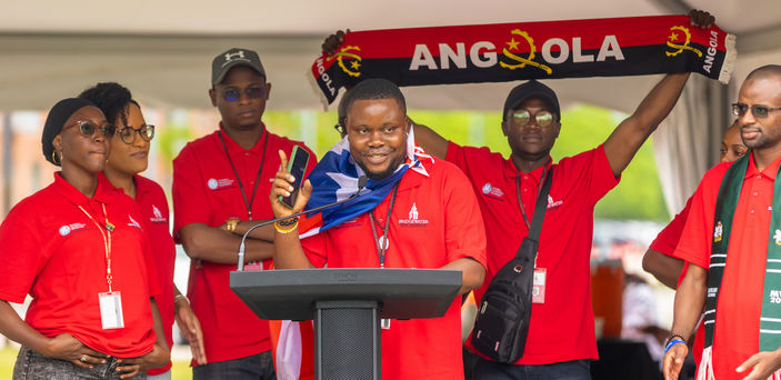 Five Mandela fellows stand in front of a podium with one holding a scarf with the word "Angola" on it.