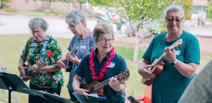 Four people play the ukulele at a Senior College event