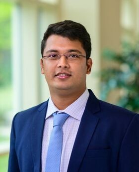 Dr. Avinandan Chakrabort with short, dark brown wavy hair wearing rimless glasses and a blue blazer over a white button up shirt with a light blue tie