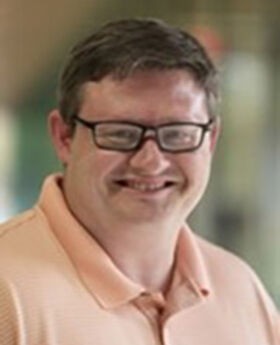 Dr. Jason Edwards smiling with short brown hair and wearing brown rim glasses and a peach colored polo shirt