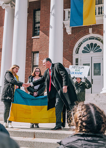 BSU President Fred Clark shaking hands with students holding the Ukrainian flag in front of Boyden Hall; a man holds a sign that says Freedom for Ukraine
