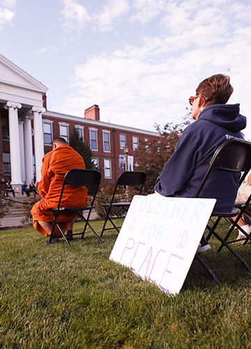 A woman sits on the lawn of Boyden Hall with a sign that says "Together for Peace"